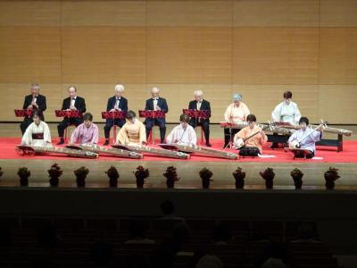 舞台上で5名の男性が尺八、2名の女性が三味線、6名の女性が琴を演奏している写真