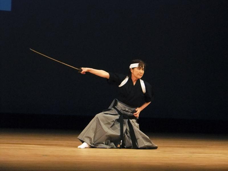 舞台の上で剣舞を披露する袴姿の女性の写真