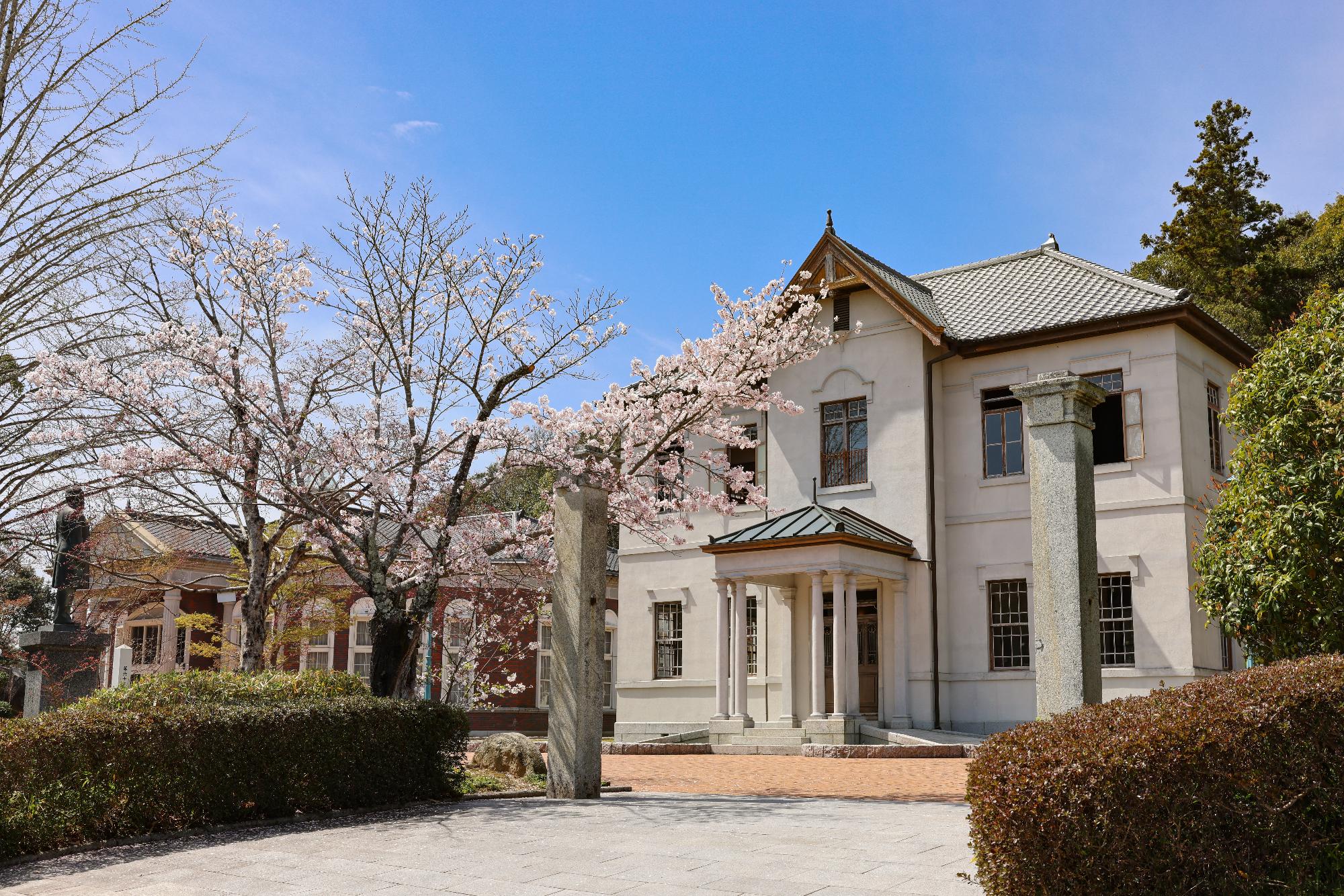 大きな木の横に建っている、白い外壁に大きな窓がある旧伊藤博文邸の写真
