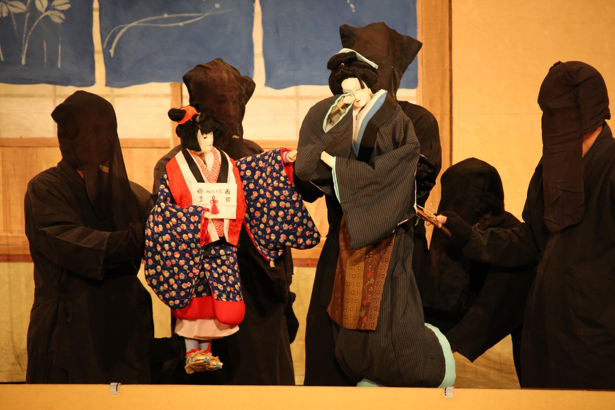舞台上で演じられている人形浄瑠璃と人形を操る黒子の写真