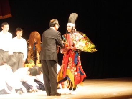 舞台で神楽部の生徒が市長から花束をもらい握手している写真