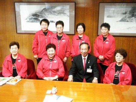 赤いウェアを着た女性が7名、市長と一緒に記念写真