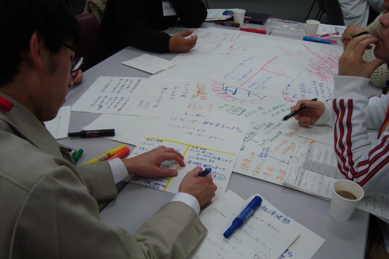 テーブルの上に置かれた資料やノートに書き込んでいる参加者の写真