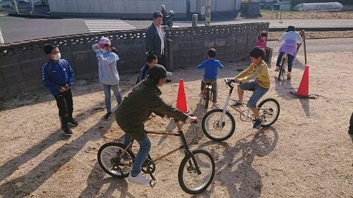 空き地で竹製の自転車に乗っている子供達の写真