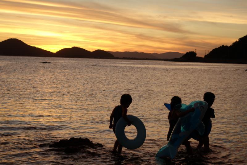 黄金色の夕焼け空と海で遊ぶ子供たちの写真