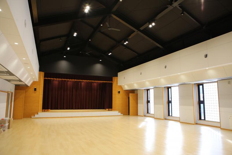 天井が高く、白い壁と大きな窓、舞台がある室積コミュニティセンターの内部の写真