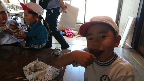 白い帽子を被りテーブルの横に座っている男の子が、嬉しそうにサツマイモを食べている写真
