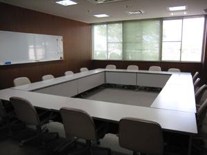 左の壁にホワイトボードが設置されて、長机をロの字に設置したところに椅子が4脚ずつ配置された会議室の内部の写真