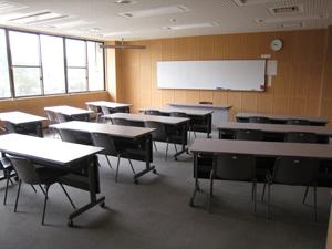 前方の壁にホワイトボードが設置してある、長机と椅子が設置された研修室の室内の写真
