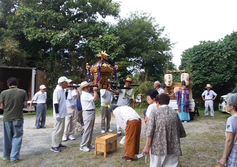 夏祭りで小さな神輿を担いでいる男性の方々の前に賽銭箱が置かれお参りをしている人々の写真