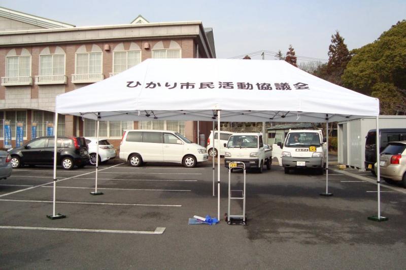 ひかり市民運動協議会とかかれた白いテントが駐車場に広げられている写真