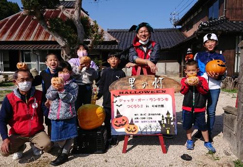 空き家の前で手作りのかぼちゃランタンを持った子ども達と川口隊員、地域住民の方の集合写真