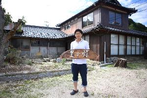 改修を行う空き家を「里の灯（あかり）」と命名し、空き家の前で看板を持っている川口隊員