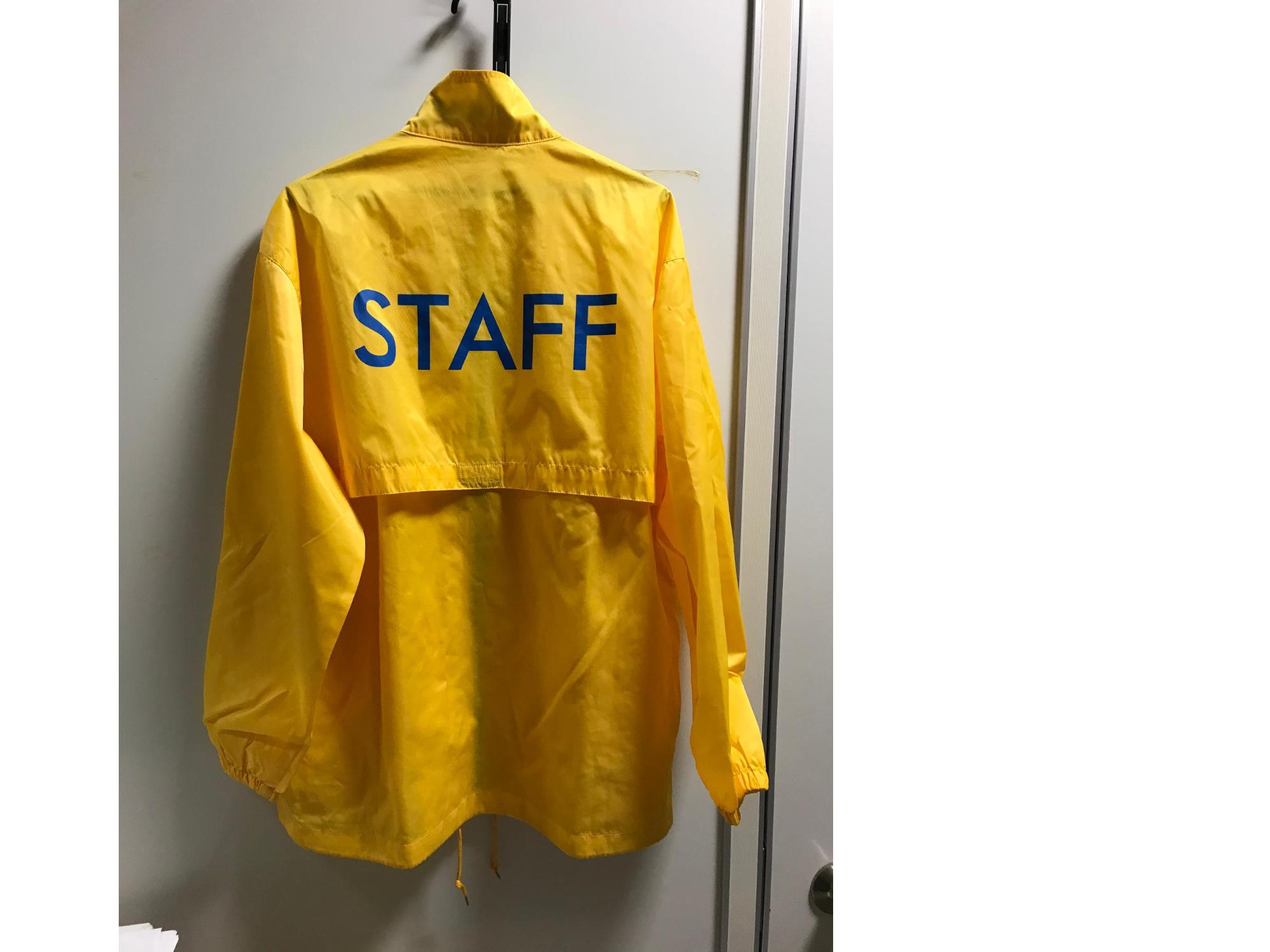 男性が着用している後ろにSTAFFを青文字で書かれた黄色いスタッフジャンパーの写真