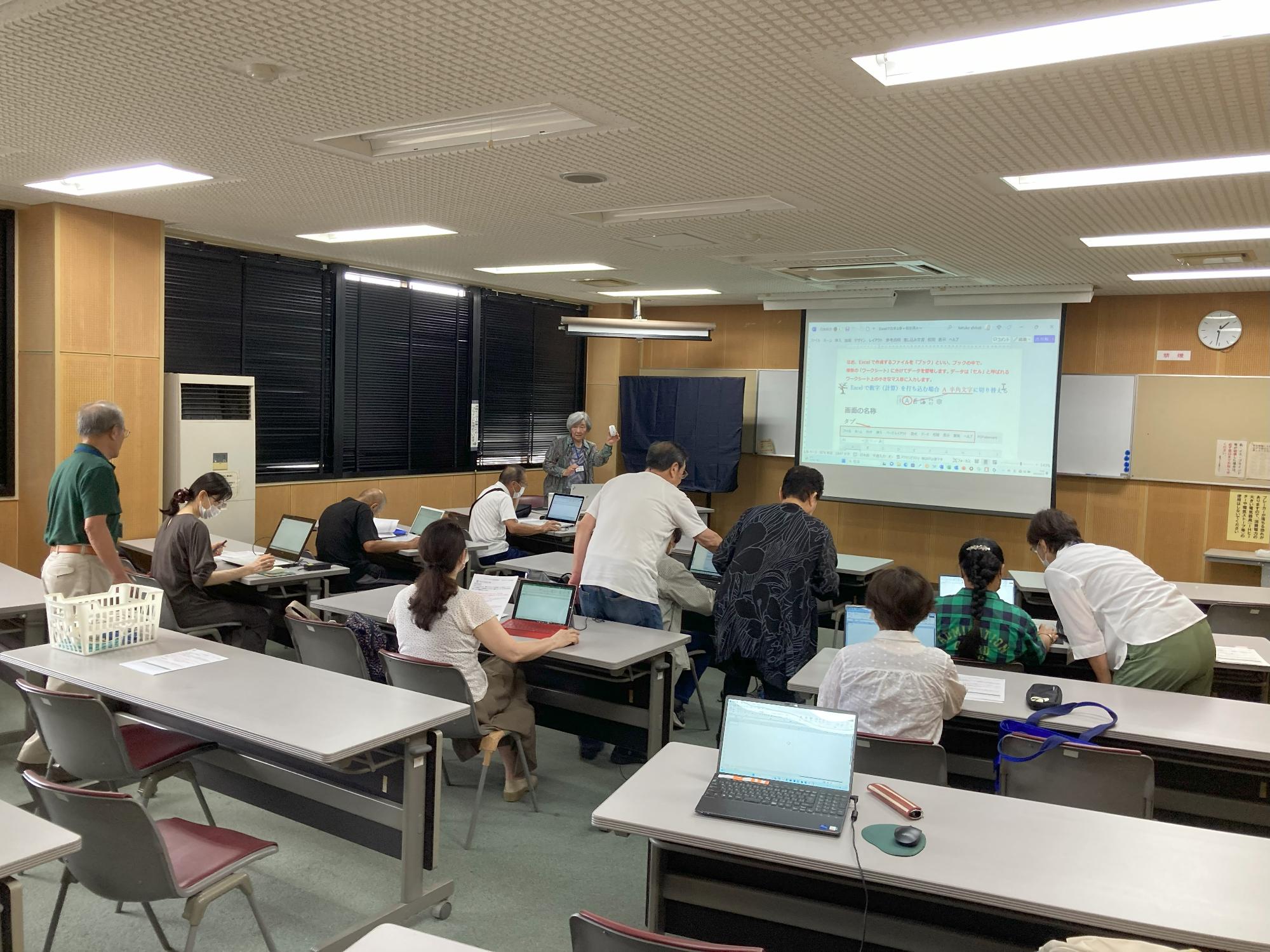前方に先生とスクリーンがあり参加者が2人1組でパソコンを見て授業を受けている写真