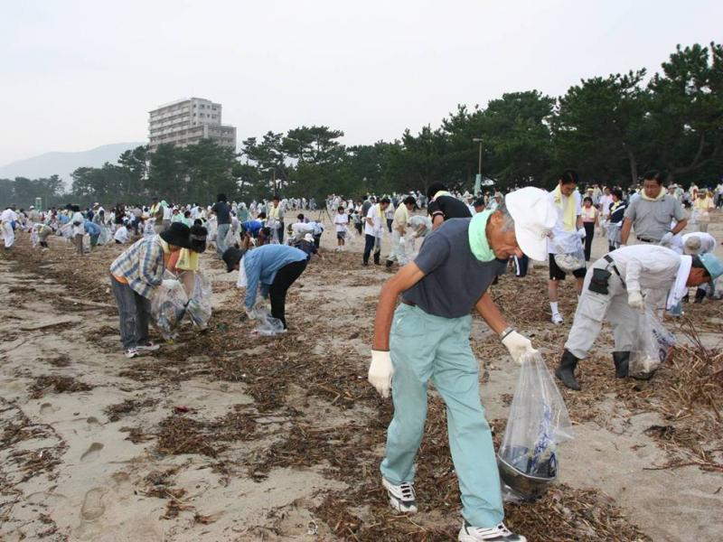 海岸で袋を片手にゴミ拾いをする大勢の人たちの写真