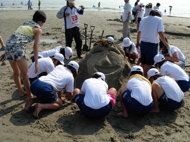 海岸で製作途中の作品の周りを取り囲みサンドアートを作る子どもたちの写真