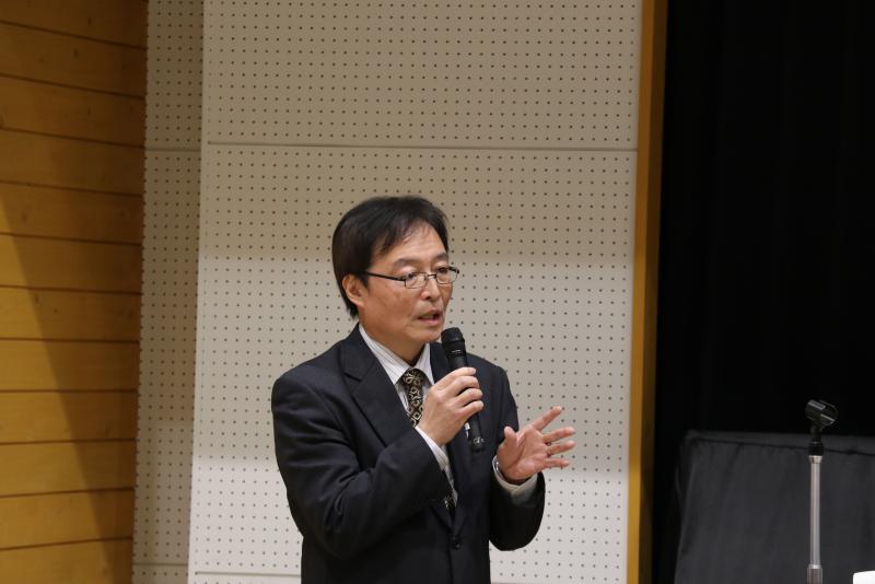 横川教授がマイクで話している写真