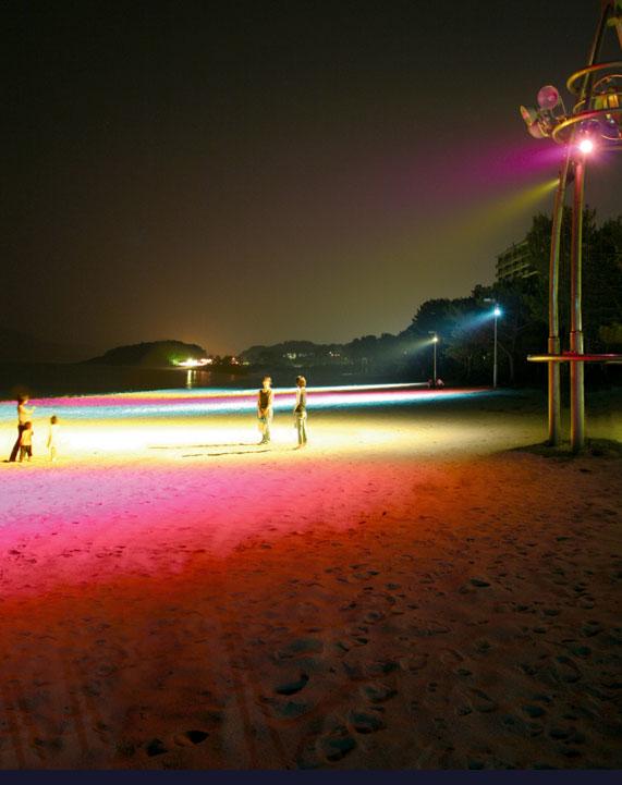 「渚のライトアップ」で虹色に輝いている虹ヶ浜海岸で楽しんでいる人達の写真