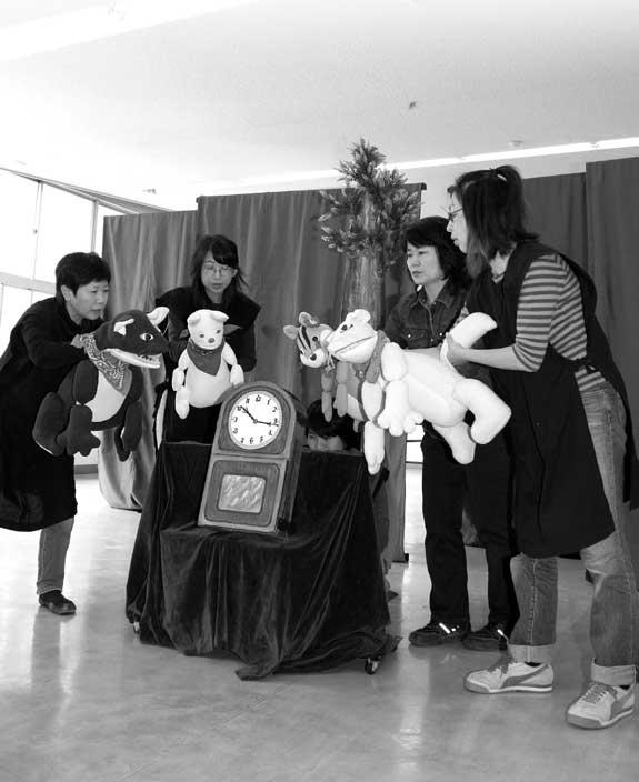 劇団員の人達4人が各自動物のぬいぐるみをもち劇中の時計の周りにたち人形劇を行っている写真