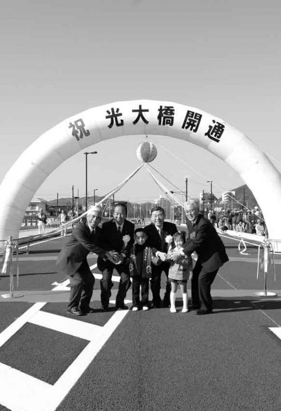 「祝 光大橋開通」の文字が書かれたアートとくす玉の前で子供と市長らが記念撮影している写真