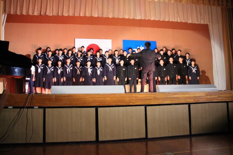 ステージの上のひな壇に立って歌う学生たちの写真