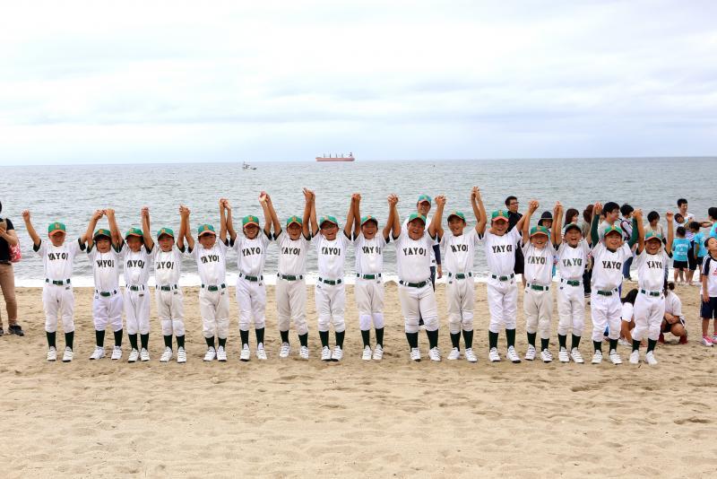 野球のユニフォームを着た子供たちが1列に並びつないだ両手を上に掲げている写真