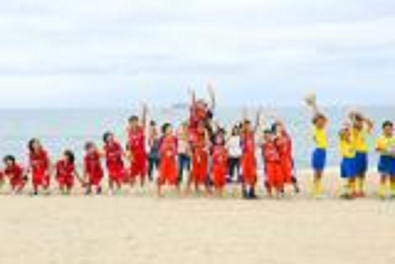 赤いユニフォームと黄色いユニフォームの子どもたちが砂浜に並んだ写真