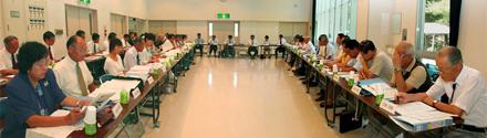 会議室で長方形型に並べられた長机で話し合っている会議参加者たちの写真1