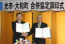 調印式で署名した文書を掲げる男性2名の写真