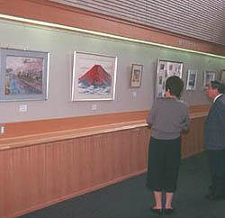 ギャラリーに飾られた朱色の山の絵を閲覧しているグレーの服を着た女性の写真