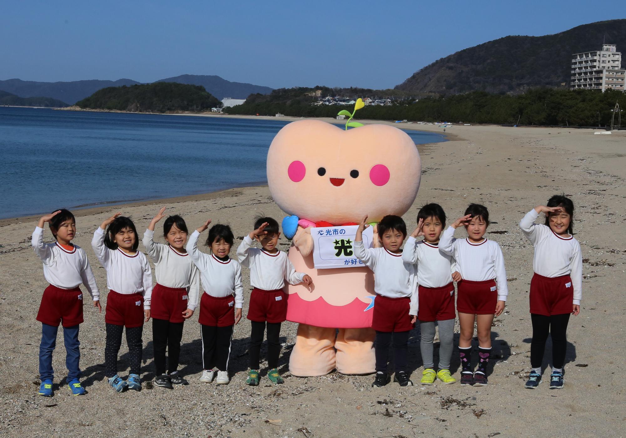 きゅっとちゃんと園児たちが虹ケ浜海岸をバックに集合写真をとっています