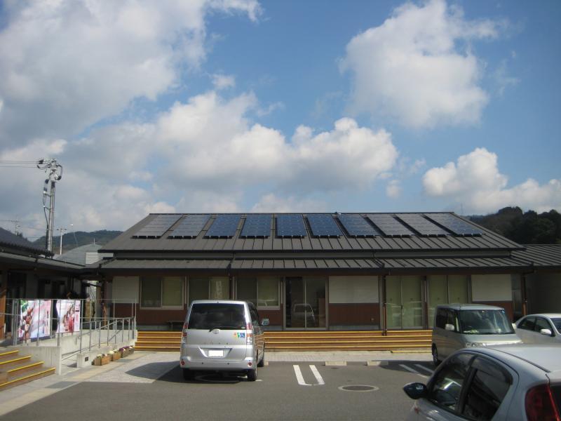 屋根の上にソーラーパネルがつている体験研修棟と駐車場に止まっている車の写真