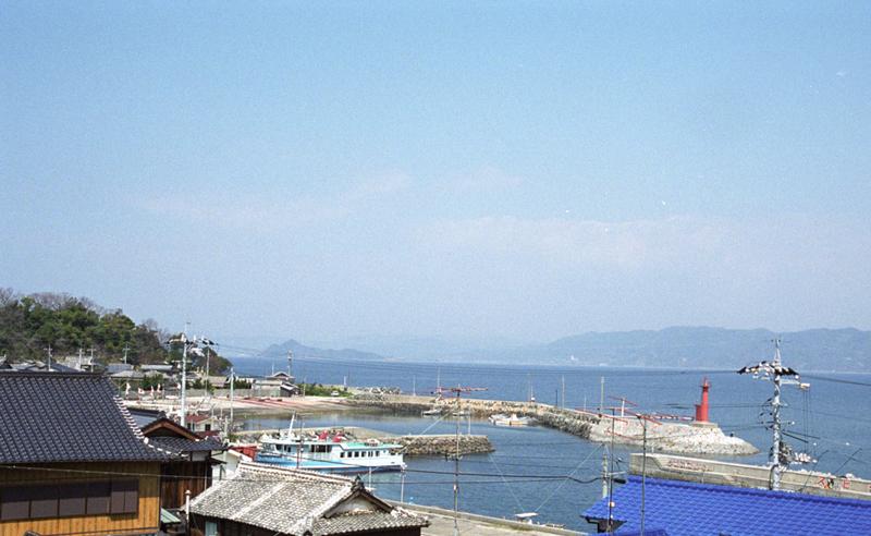 遠くに見える島と青い屋根の間にある赤い灯台が目印のカーブを描いている港の写真