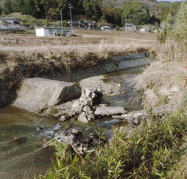 水嵩の引いた川と中央で崩れた頭首工の写真