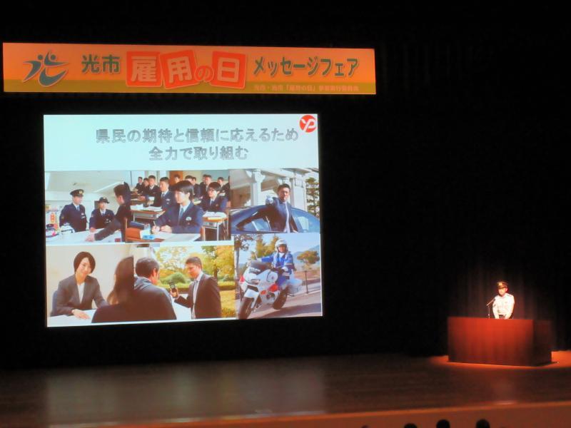 ステージ上のスクリーンに山口県光警察署のプレゼンのスライドが映し出されている写真