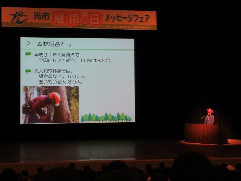 ステージ上のスクリーンに光大和森林組合の紹介スライドが映し出されている写真