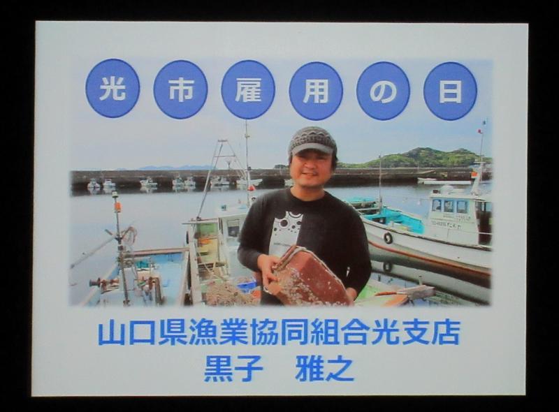 漁船を背景に、カメラに向かって笑顔を見せる黒子さんの写真