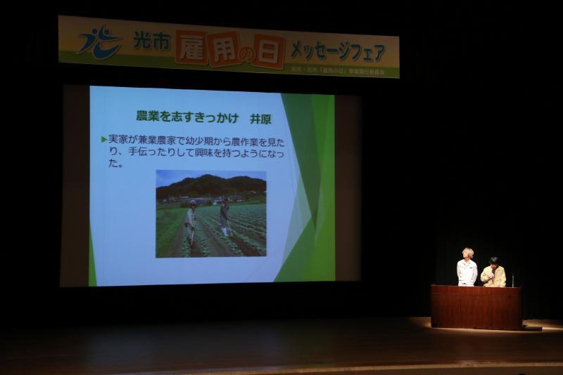 ステージ上のスクリーンに「農業を志すきっかけ」と題されたスライドが映し出されている写真