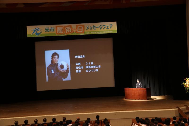 ステージ上のスクリーンにイワヤケイスケさんの紹介が映し出されている写真