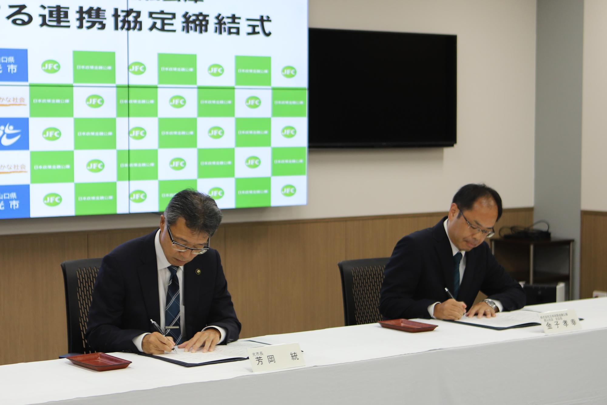 連携協定締結式で芳岡市長と日本公庫徳山支店の金子支店長が協定書に署名している様子