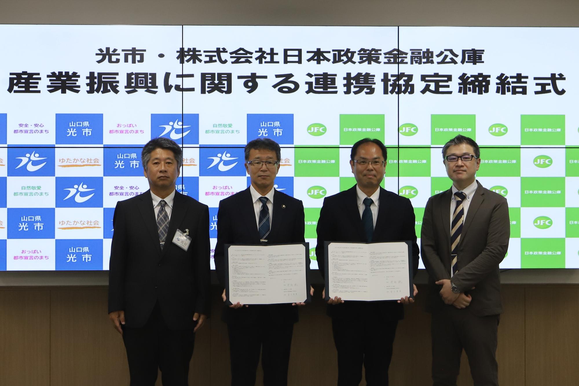 芳岡市長、西村経済部長、日本公庫徳山支店の金子支店長、白土融資課長が協定書を手に記念撮影を行っている様子