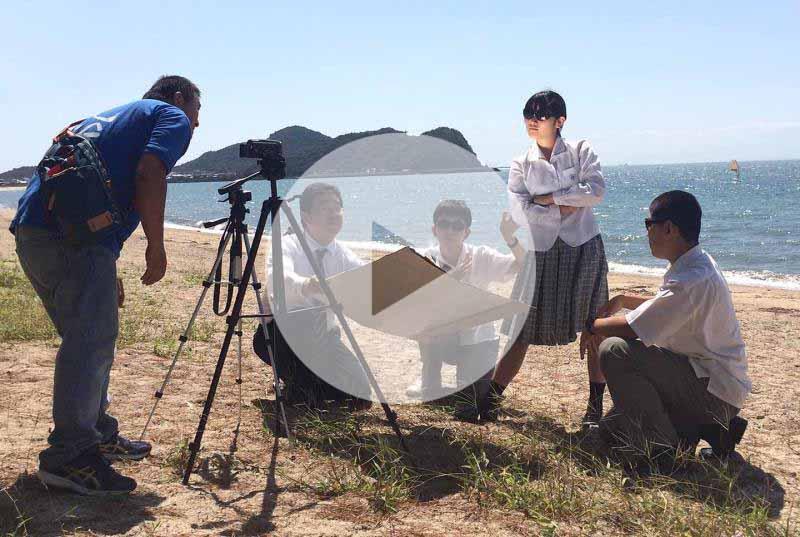 海辺で複数の人が三脚とカメラで映像を撮っている(動画のスクリーンショット)(YouTube動画へのリンク)