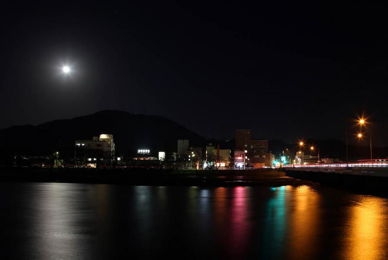 月の光と、街の光が反射し、島田川に写る虹色の光の写真