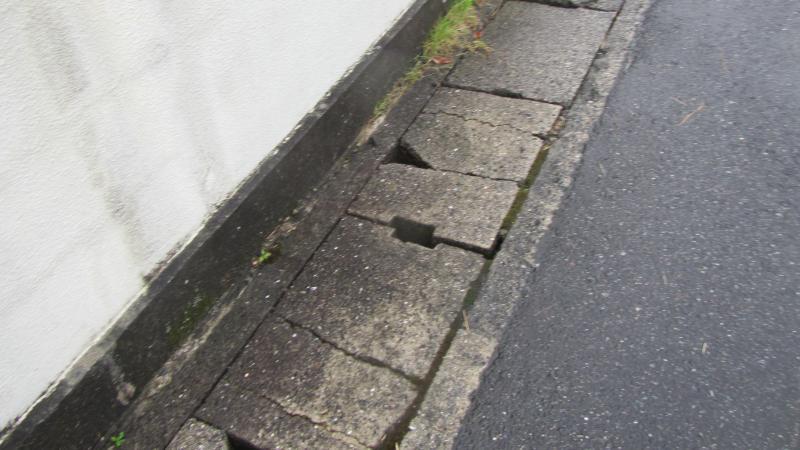 コンクリートの一部が三角形に欠けたりヒビが入っている側溝の蓋の写真
